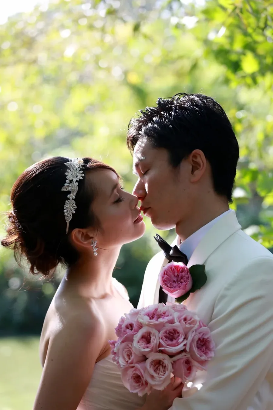 A couple leaning in to kiss, the bride holding pink roses
