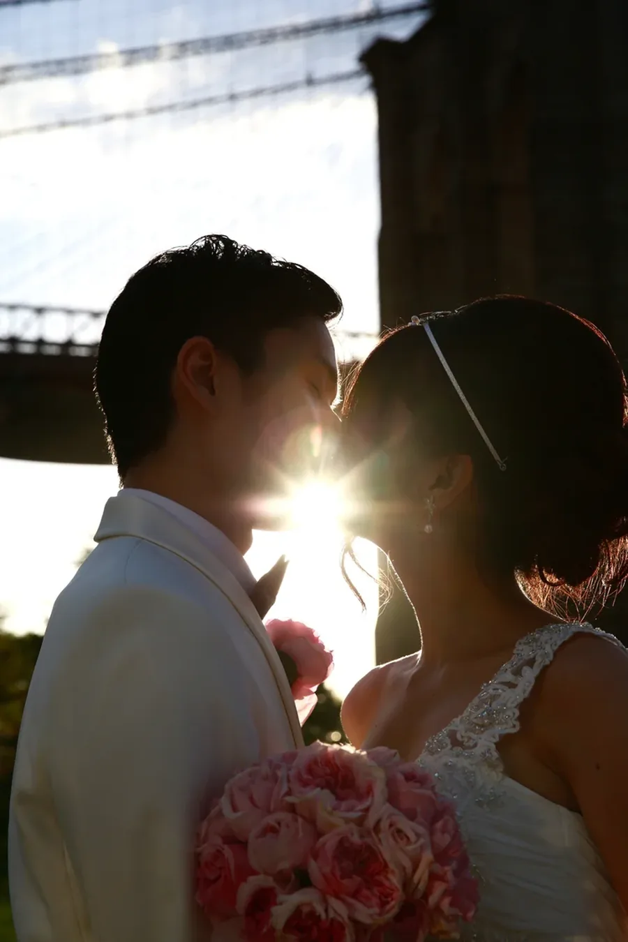 A couple kissing beneath the Brooklyn Bridge as the sun sets behind them