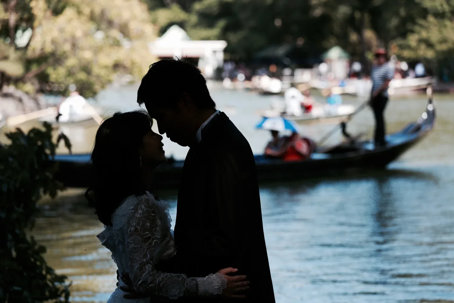 A couple in silhouette beside the lake as a gondola passes behind them