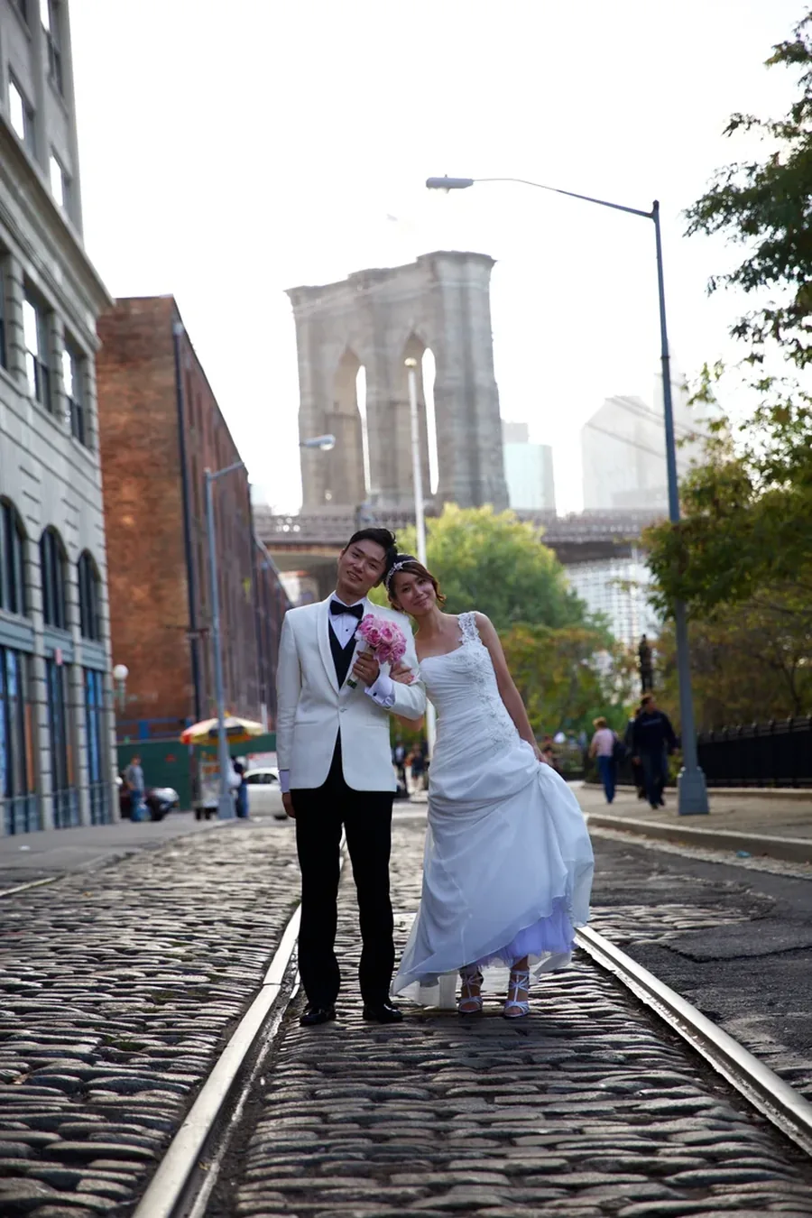 A couple standing on the cobblestones of Dumbo beneath the Brooklyn Bridge