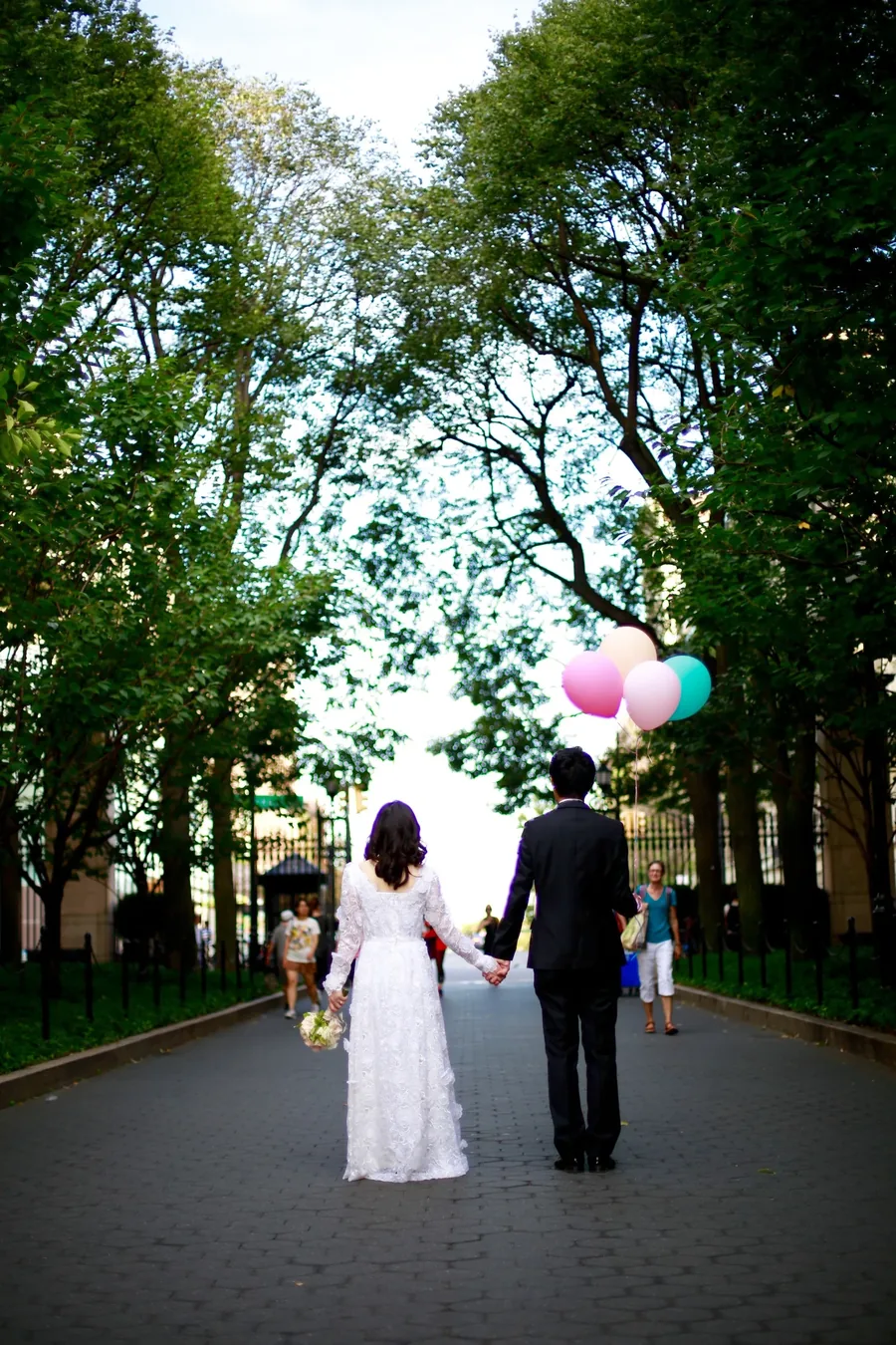 A couple walking away down a tree lined path, carrying balloons